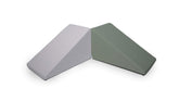 Two durable Mega Wedge Play Triangles by Foamnasium are positioned side by side. The cushion on the left is light gray and the one on the right is olive green. Both have a triangular shape with a slope, and they rest against each other at their widest points. These CertiPUR-US certified cushions ensure safety and comfort.